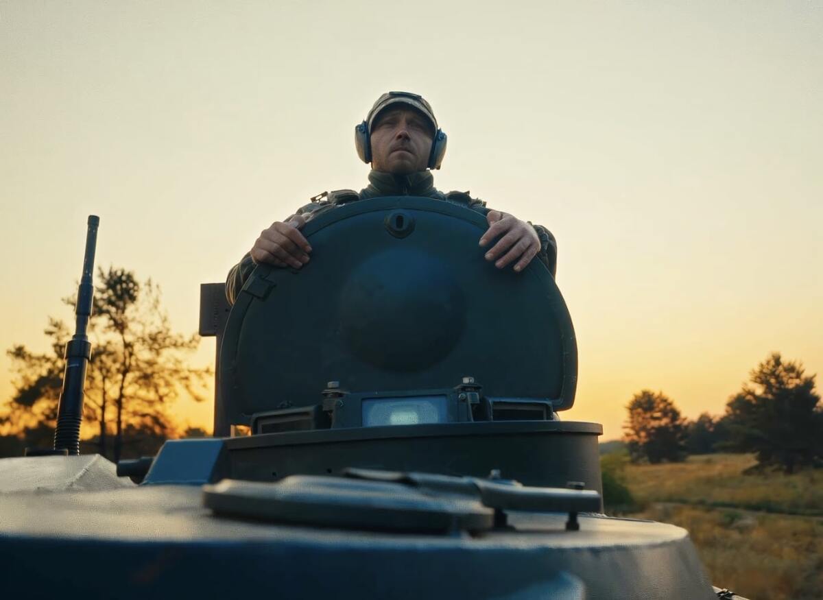 Боєць виглядає з люка танка на фоні заходу сонця
